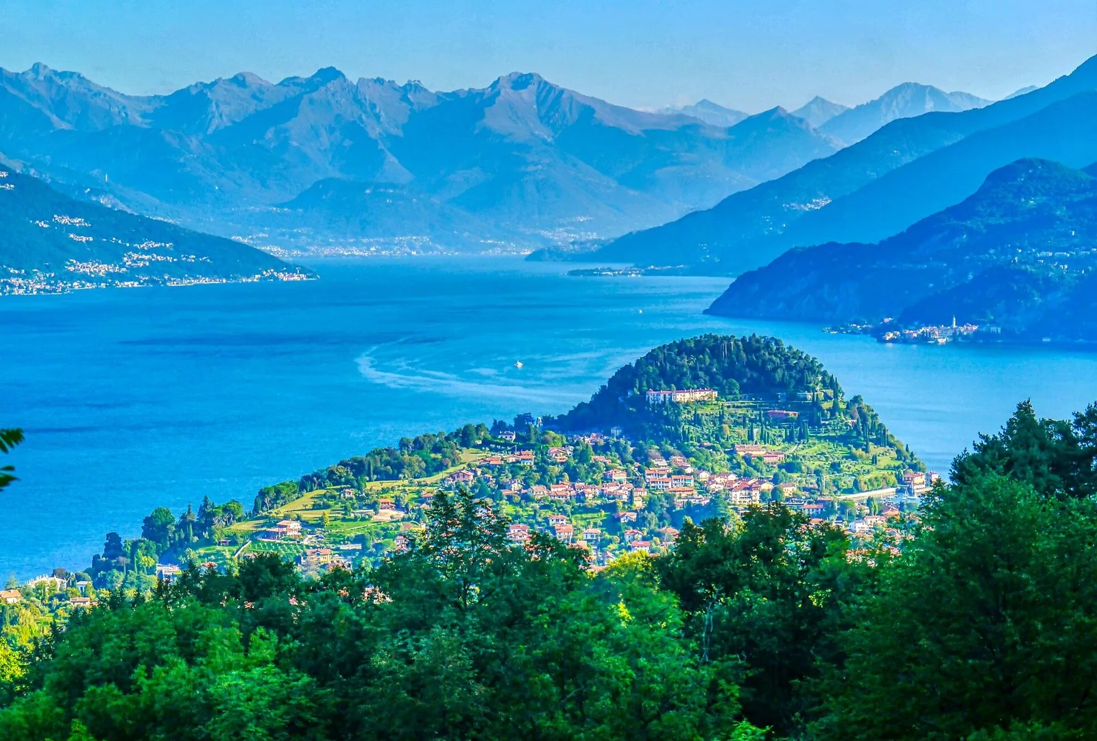 Veduta dall'alto del promontorio di Bellagio con il borgo e la collina boscosa, il lago azzurro e le montagne sullo sfondo