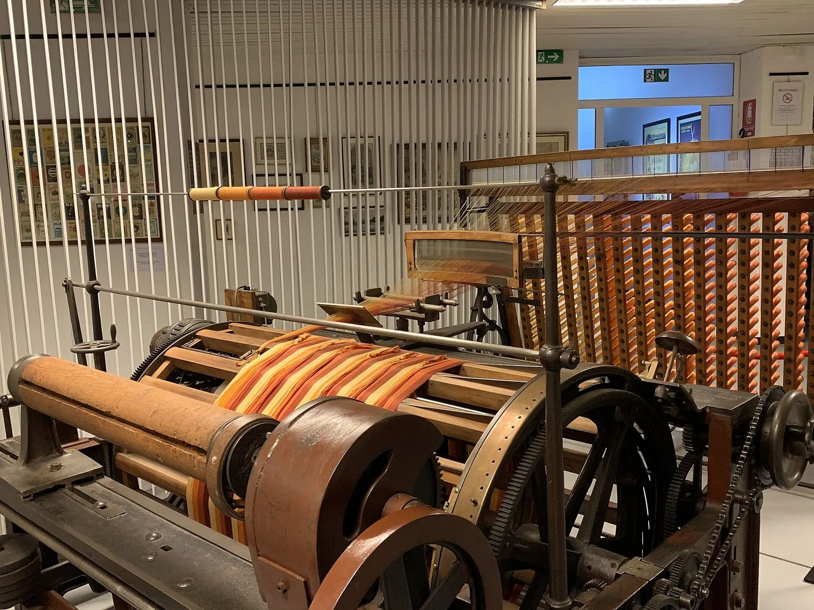 Un macchinario tessile storico in legno e metallo con fili e rocchetti arancioni esposto in una sala del Museo della Seta di Como